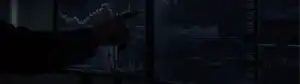 Person pointing at trading charts on multiple dark screens