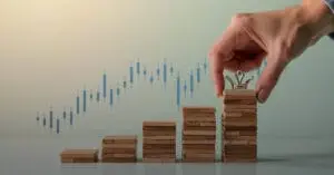 Hand places a chess king on stacked blocks with a rising stock chart, symbolizing success and growth.