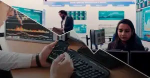 Multiple professionals monitor financial data on computers and phones in a trading office with screens showing charts and market statistics