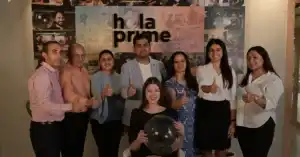 Smiling team posing together indoors with thumbs up, standing in front of hola prime logo.